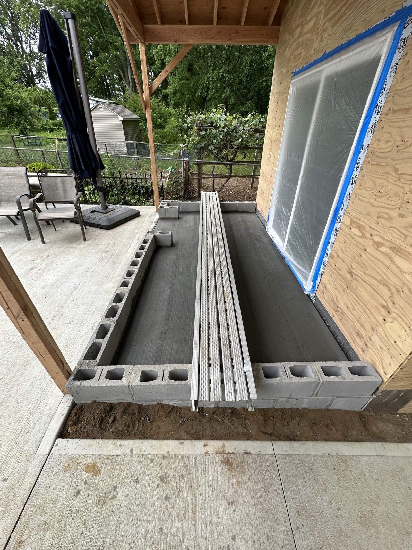 Fresh concrete slab poured inside block foundation with covered porch framing