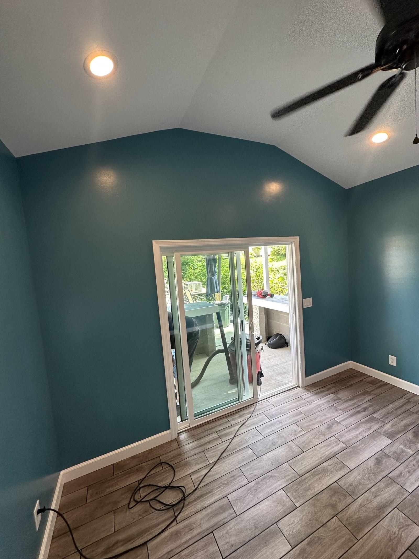 Finished pool house interior with sliding door, vaulted ceiling, and wood-look flooring